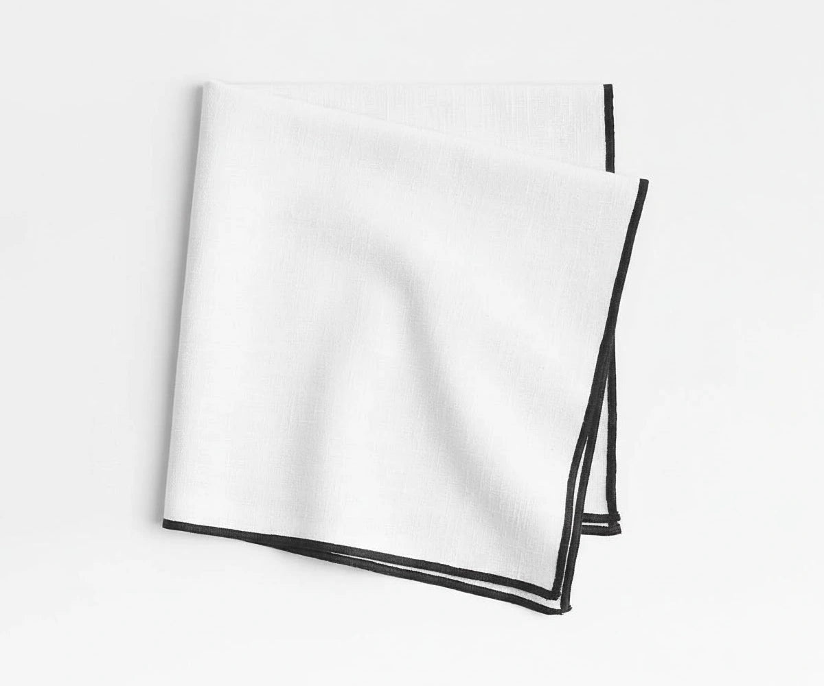 White merrow stitch cotton napkins with black border styled on modern dining table, minimalist embroidered cloth napkins for farmhouse, festive, and contemporary table décor.