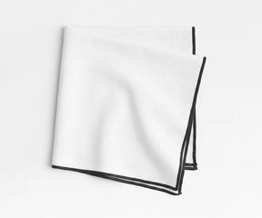White merrow stitch cotton napkins with black border styled on modern dining table, minimalist embroidered cloth napkins for farmhouse, festive, and contemporary table décor.