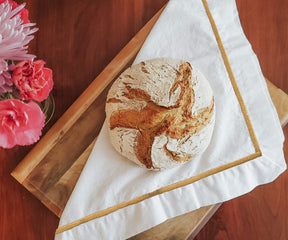 White cloth napkins displayed near a loaf of bread and flowers