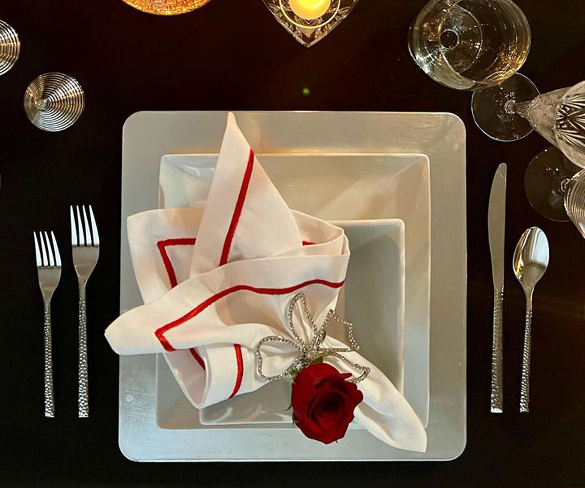 Place setting with a red rose and a white dinner napkin on a plate.