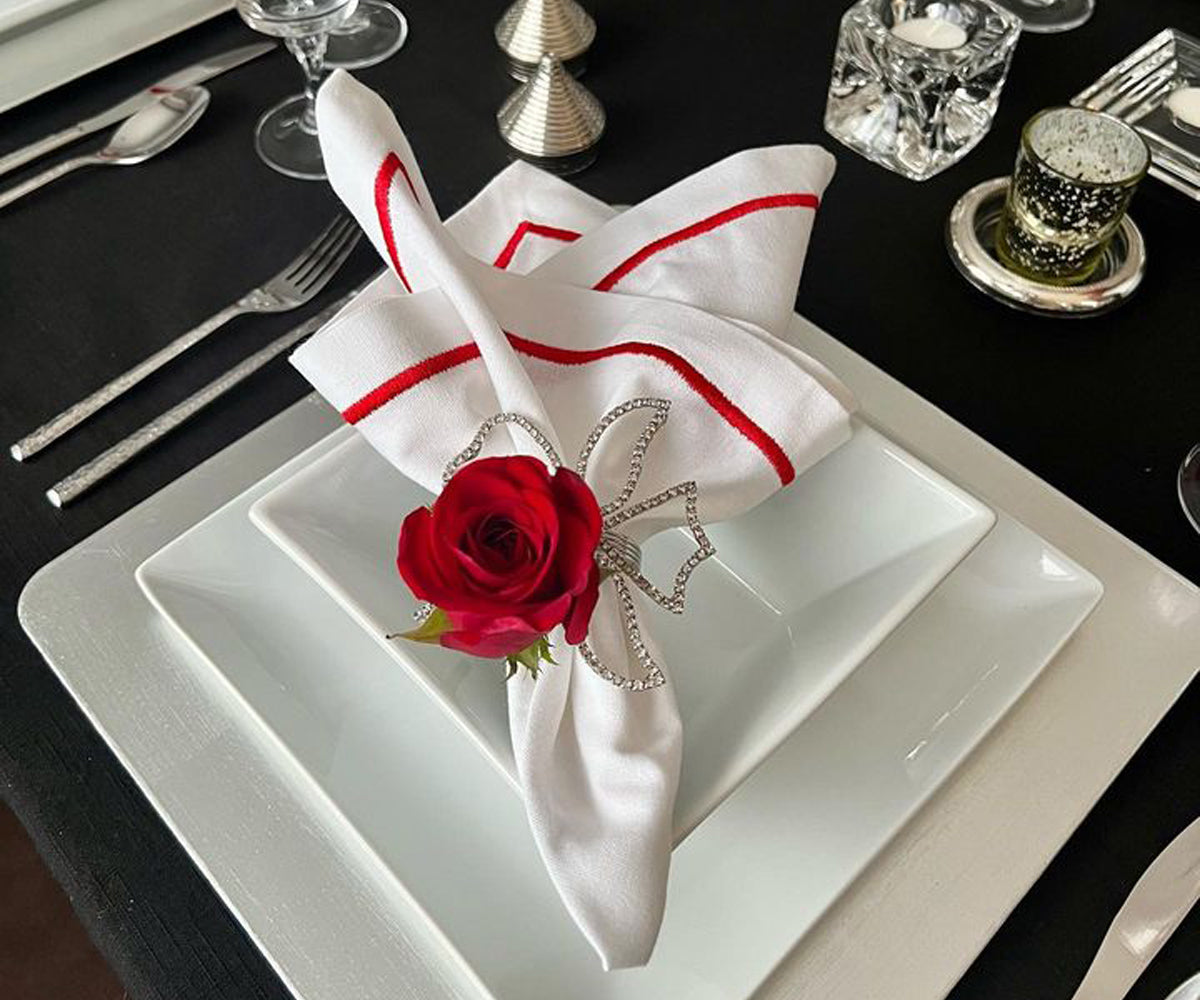 Place setting with a red rose and a white cloth napkin on a plate
