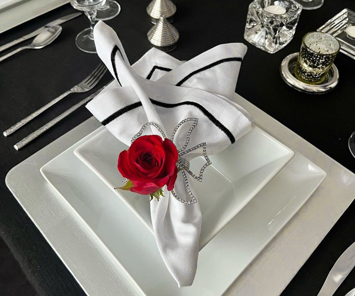 Elegant black cloth napkins arranged on a table with a single red rose centerpiece