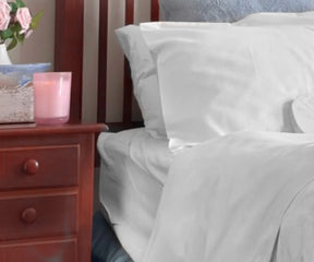 Bed with white cotton fitted sheets and a nightstand with a vase of flowers