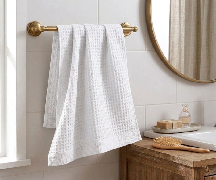 White waffle weave cotton bath towel hanging on a brass towel bar in a modern rustic bathroom.