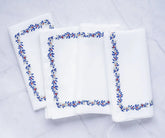 Set of white cotton napkins with a refined stitched leaf border design in blue, red, and soft grey, adding a classic touch to any table setting.