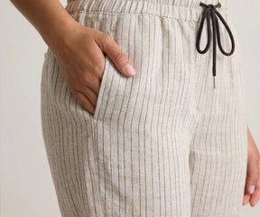 Close-up of a person wearing beige striped pants with a drawstring on a plain background