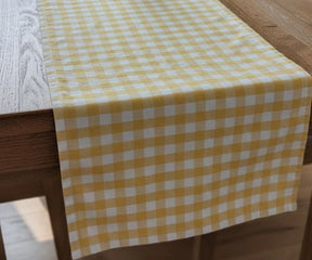 A yellow and white gingham checkered table runner draped over a wooden dining table.