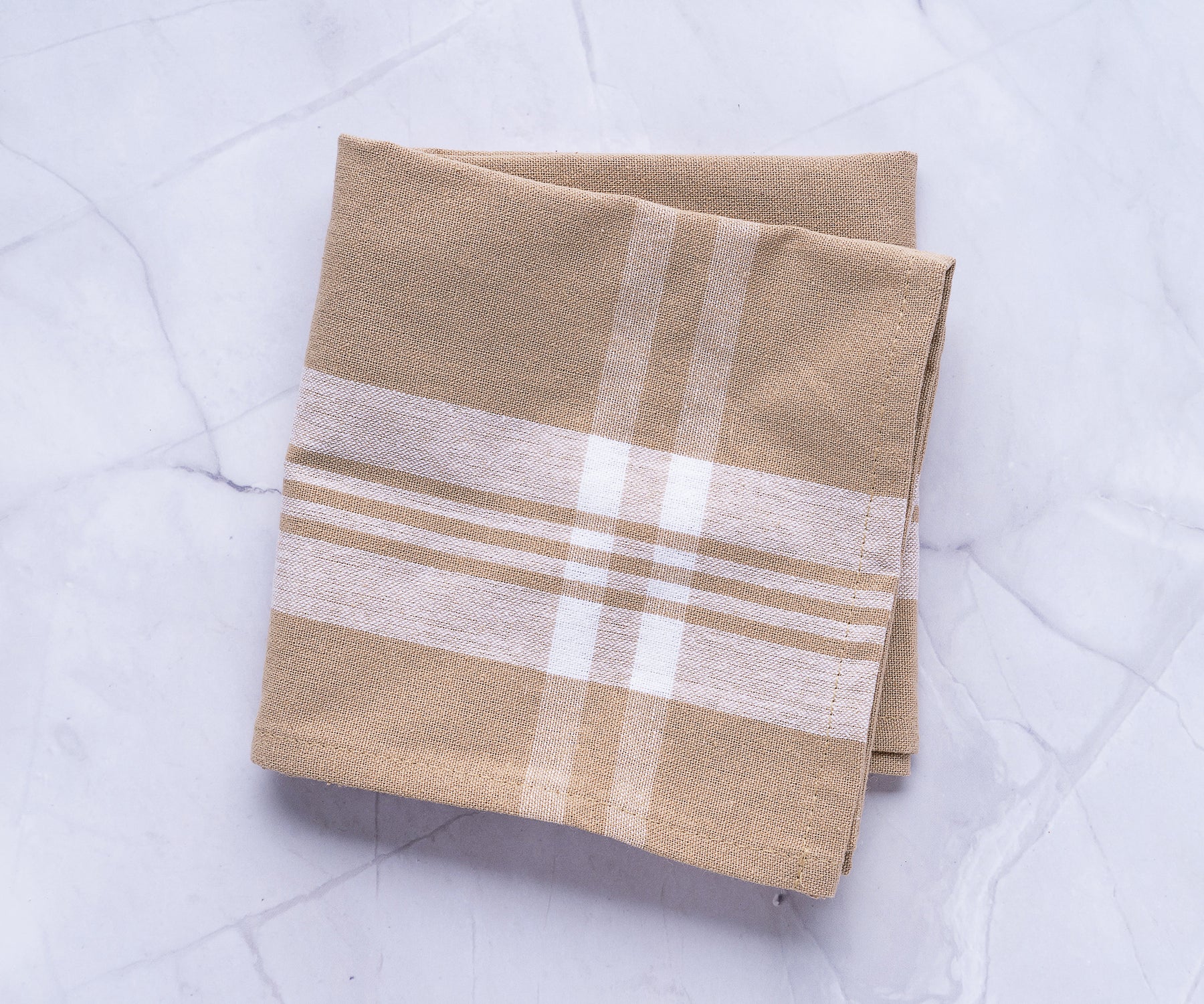 A brown and white plaid farmhouse kitchen towel on a textured marble surface