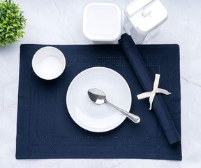 Folded rectangular placemats of size 13×18", hem stitched navy blue table placemats are placed on the plate with cups .