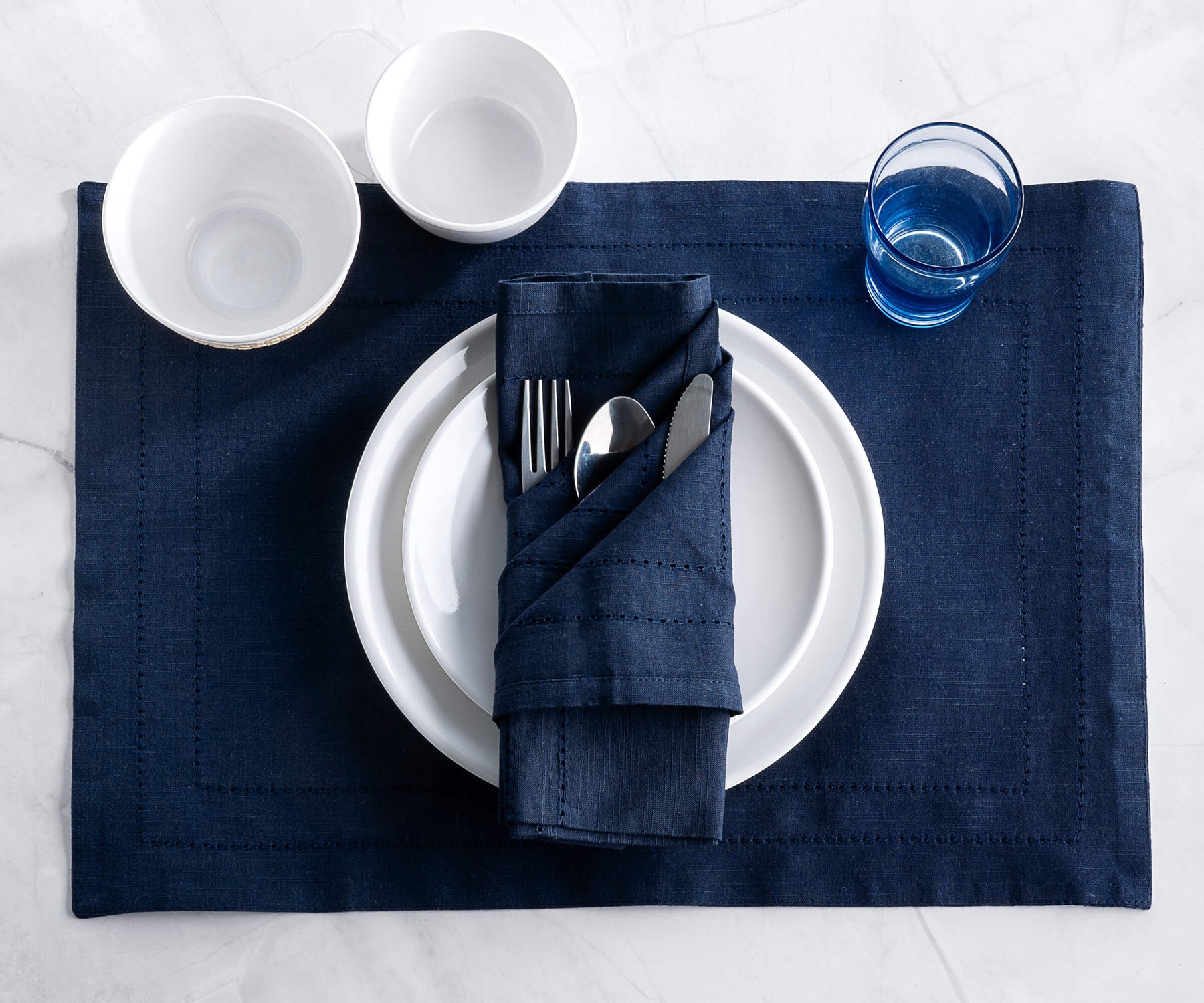 Folded rectangular placemats of size 13×18",hem stitched navy blue table placemats are placed on the plate..