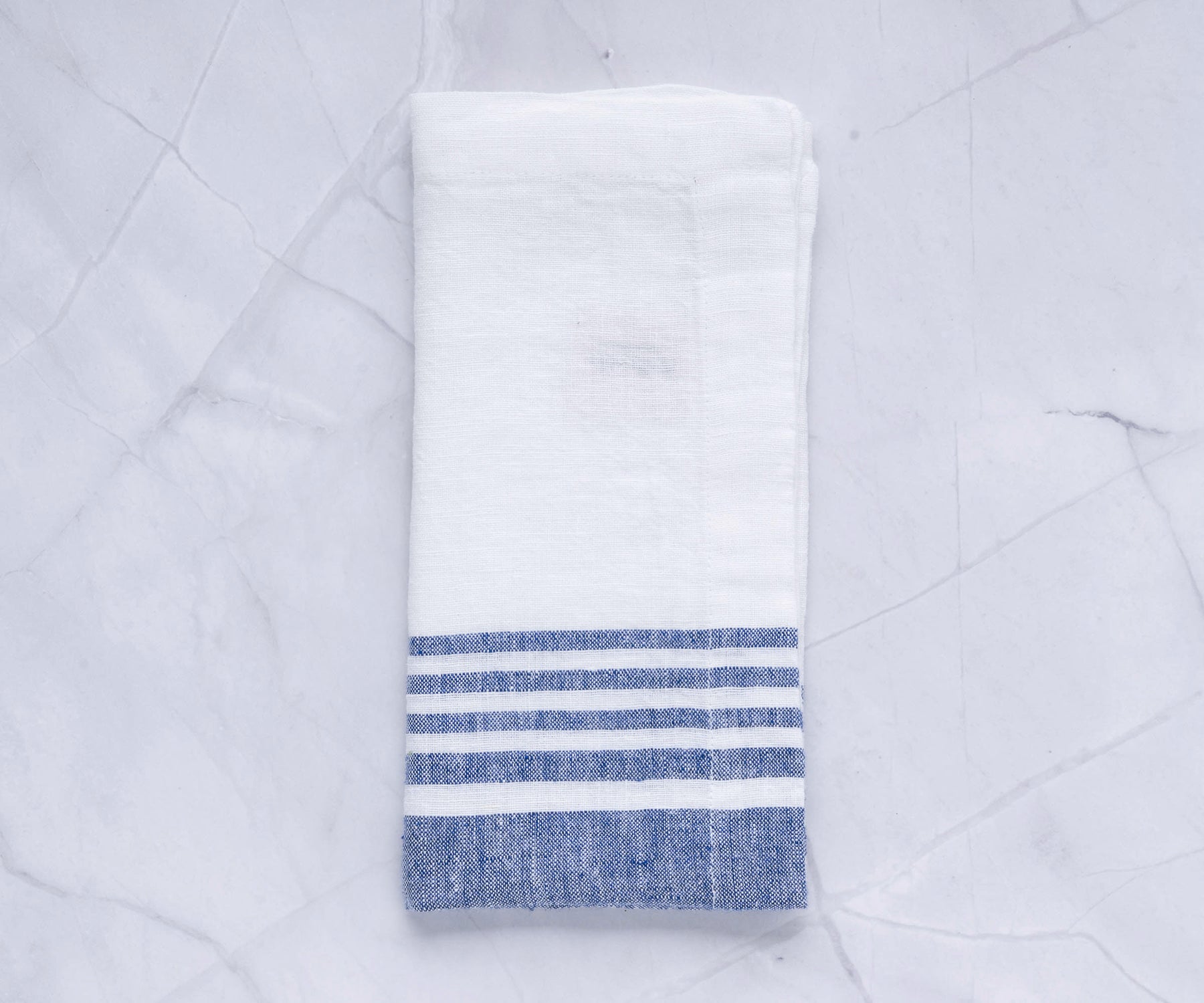 One linen dinner napkin with blue stripes on a marble countertop