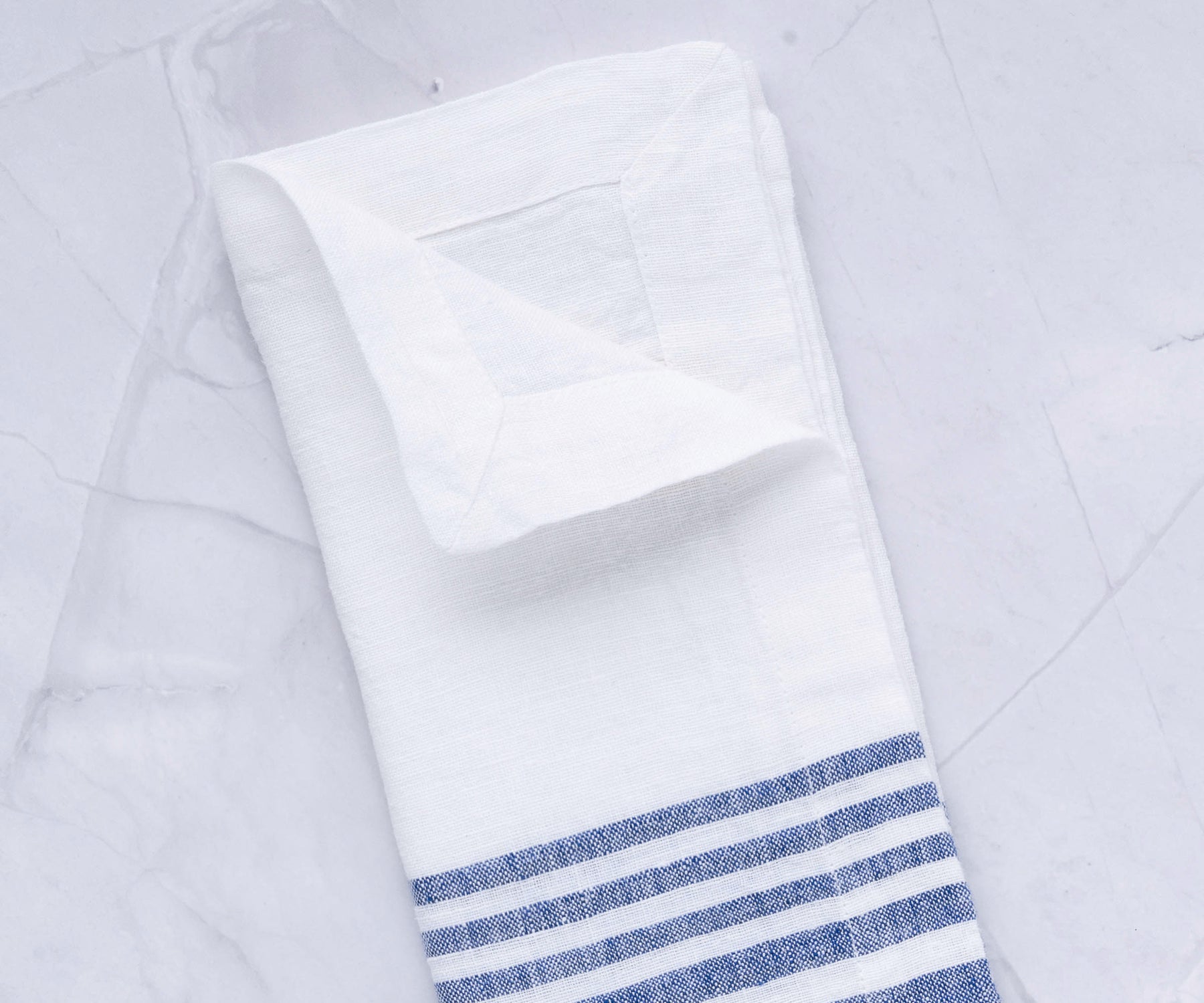 Linen dinner napkin with blue stripes arranged on a marble countertop