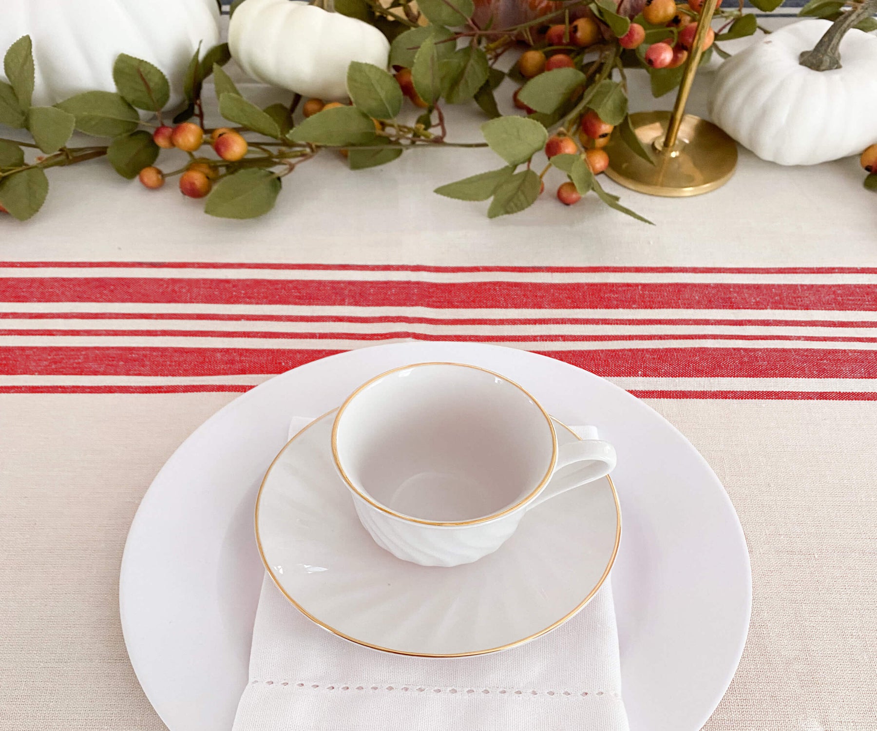 Table setting featuring a white plate, gold cup, and a red and white striped farmhouse tablecloth
