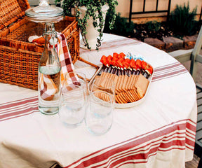 Round outdoor tablecloth displayed on a table with assorted food and beverages
