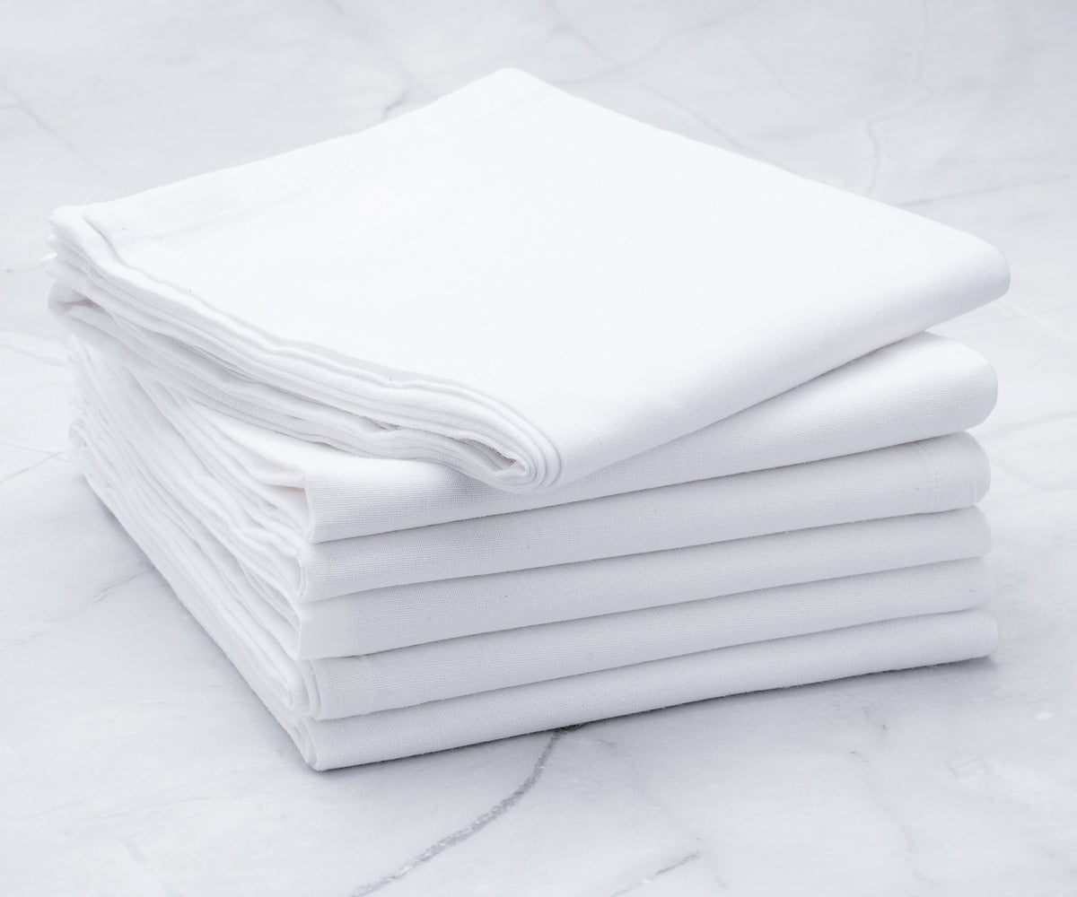 White flour sack kitchen towel spread out on a wooden countertop with baking essentials.
