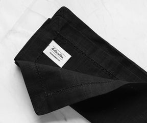 Hemstitched folded dark black cloth napkins with 1" borders with the label of All cotton and linen.