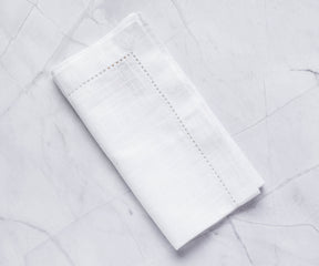 white napkins with 1" borders are folded and hemstitched pattern white linen napkins are placed on the white surface
