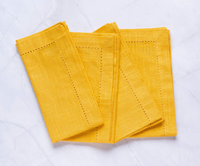 Hemstitched Folded yellow cloth napkins with 1" borders are arranged alternately.