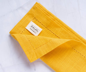 A folded yellow cloth dinner napkins with the label of All cotton and linen.