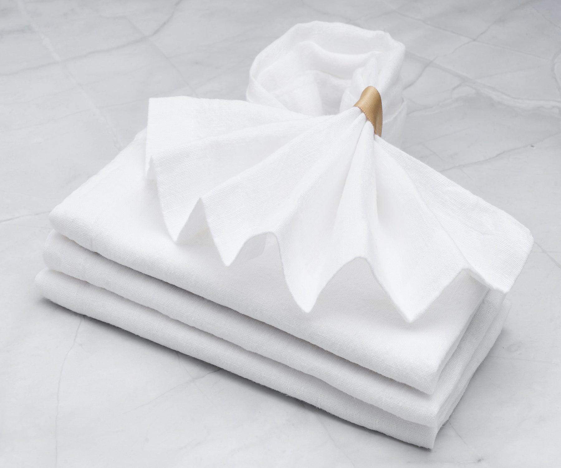 Neatly stacked white linen napkins on a marble countertop