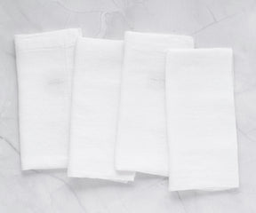 Set of four white linen napkins displayed on marble