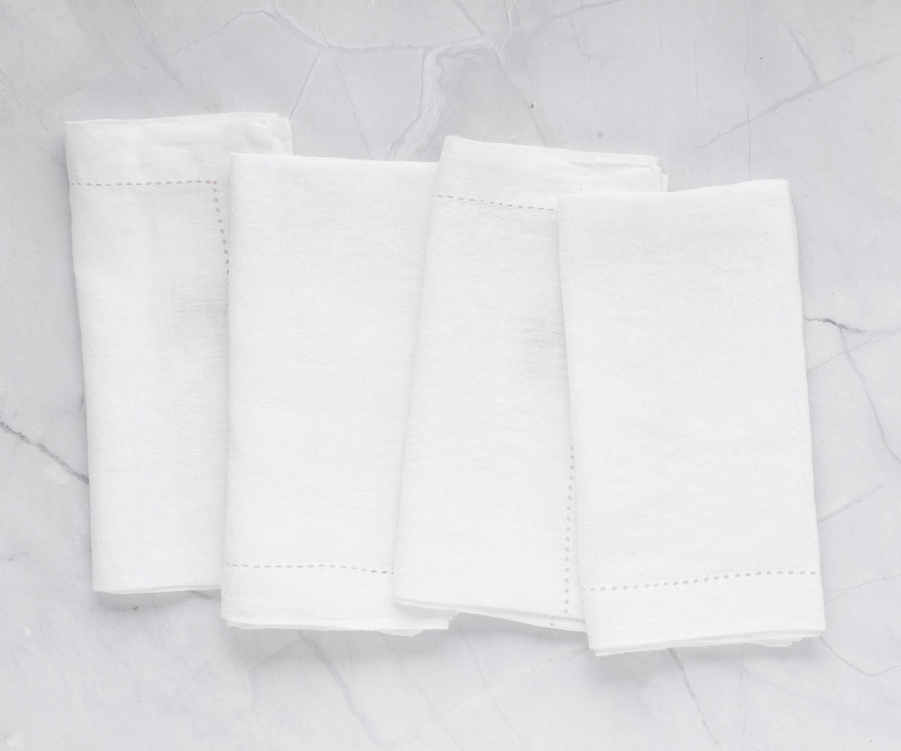 Group of four elegant white linen napkins on a marble background