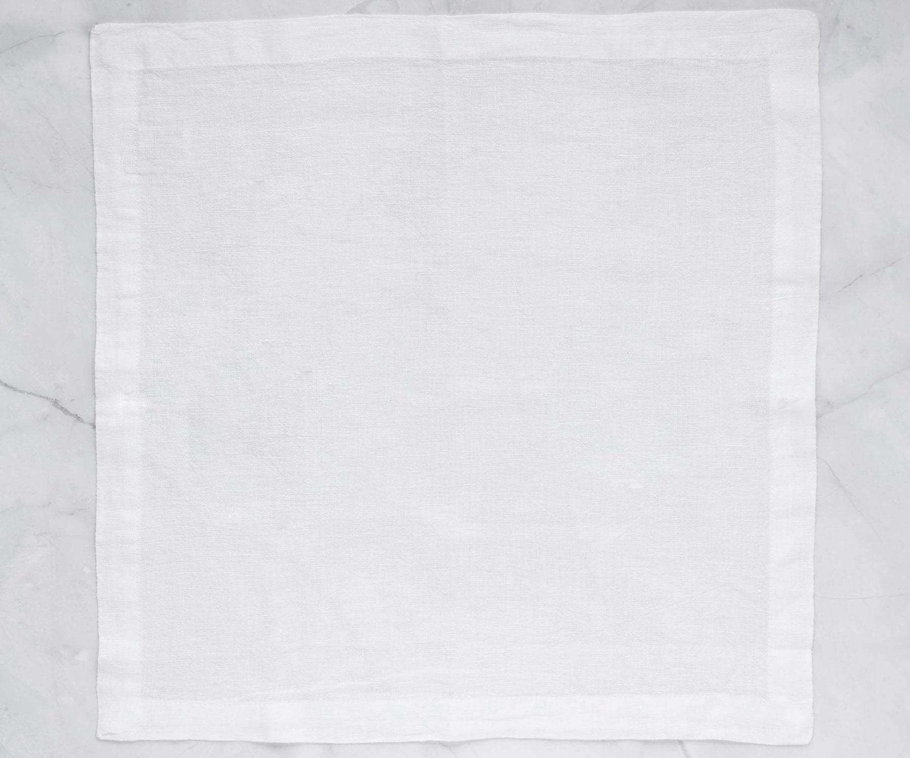 Single white linen napkin laid out on a marble surface