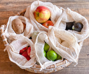 Assorted fruits and vegetables inside a reusable mesh produce bag.